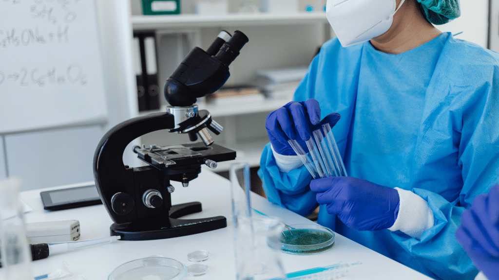 Laboratory technician holding test tubes next to microscope for clinical drug test confirmation